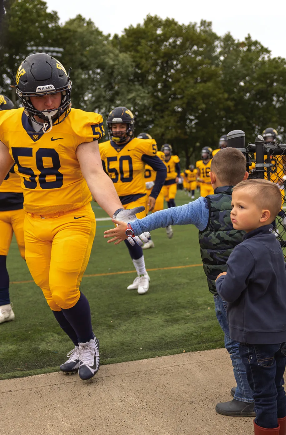 Wilkes football players giving handshakes to two small kids