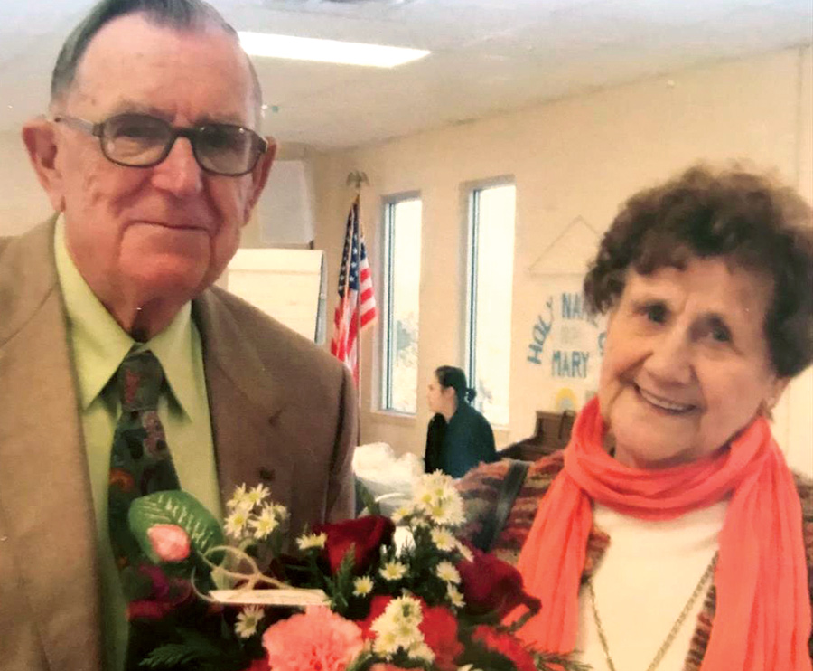 Leonard Kurello and Sabina Helen Kurello (of Forest, Va.) smile and pose for a picture together smiling for their 70th wedding anniversary as Leonard is wearing a tan colored suit and green button-up dress shirt with multi-colored tie while Helen is wearing a multi-colored cardigan with pink colored scarf holding some flowers at Holy Family Catholic Church in Sugar Notch, Pa.
