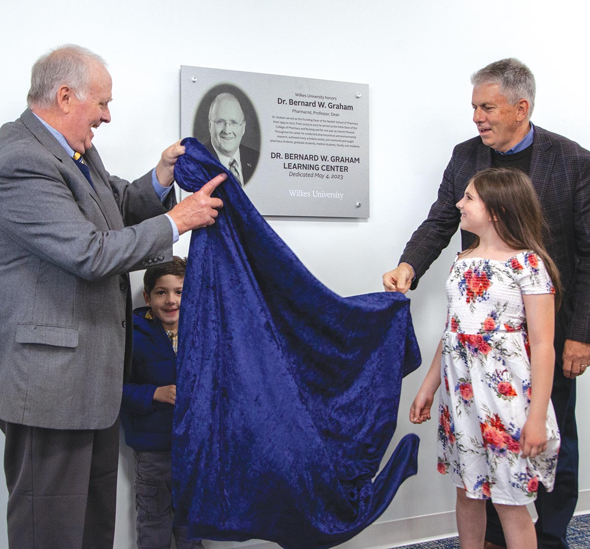 Dr. Bernard W. Graham unveils the plaque in the Graham Learning Center building at Wilkes University with the help of another man and two other children nearby him
