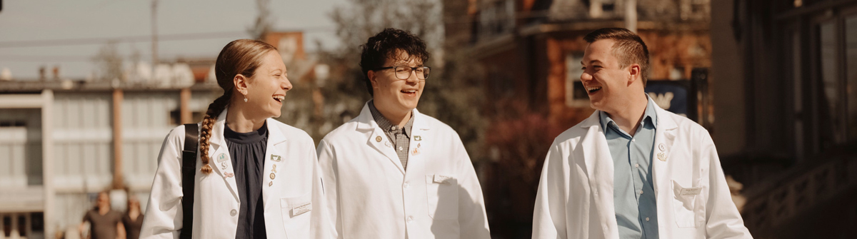 Three people in white lab coats walking and smiling outdoors.