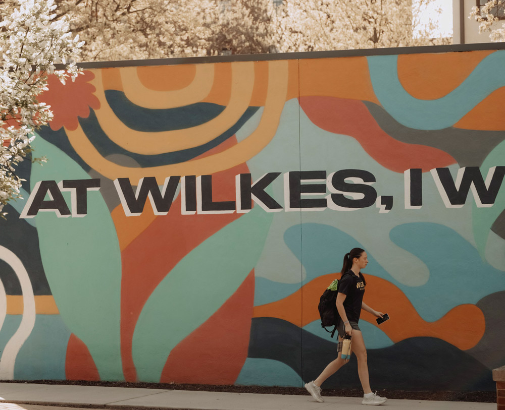 A person walks past a colorful mural with abstract patterns and bold text.