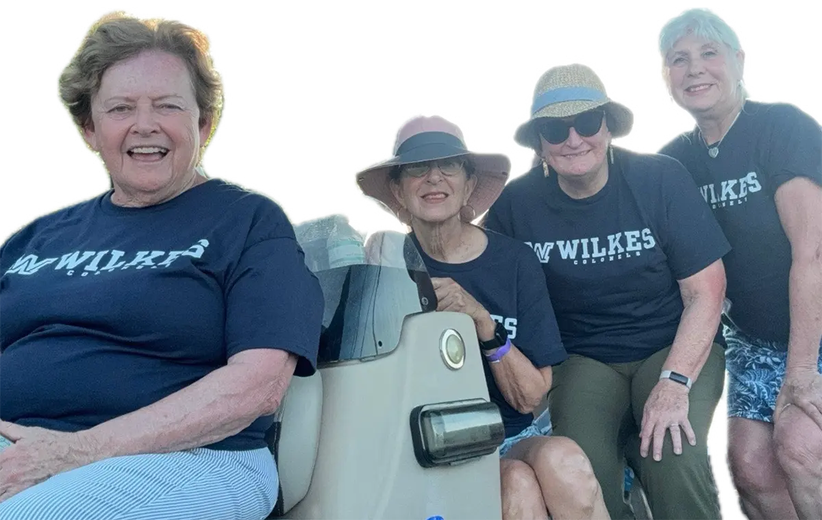 Landscape orientation photograph of Judy (Greenstein) Davis alongside her friends Bonnie (Marconi) Evans ’72, Joanne Sullivan ’73 and Karen (Dryska) Kelly ’74 for a weekend reunion at her home on Lay Lake, Alabama; Judy hosted her friends as she, Joanne and Karen all lived in Chapman Hall while Bonnie lived in Wilkes-Barre; Unbroken bonds continue after all these years! In this particular photograph, they are all seen smiling in their Wilkes Colonels logo branded t-shirts