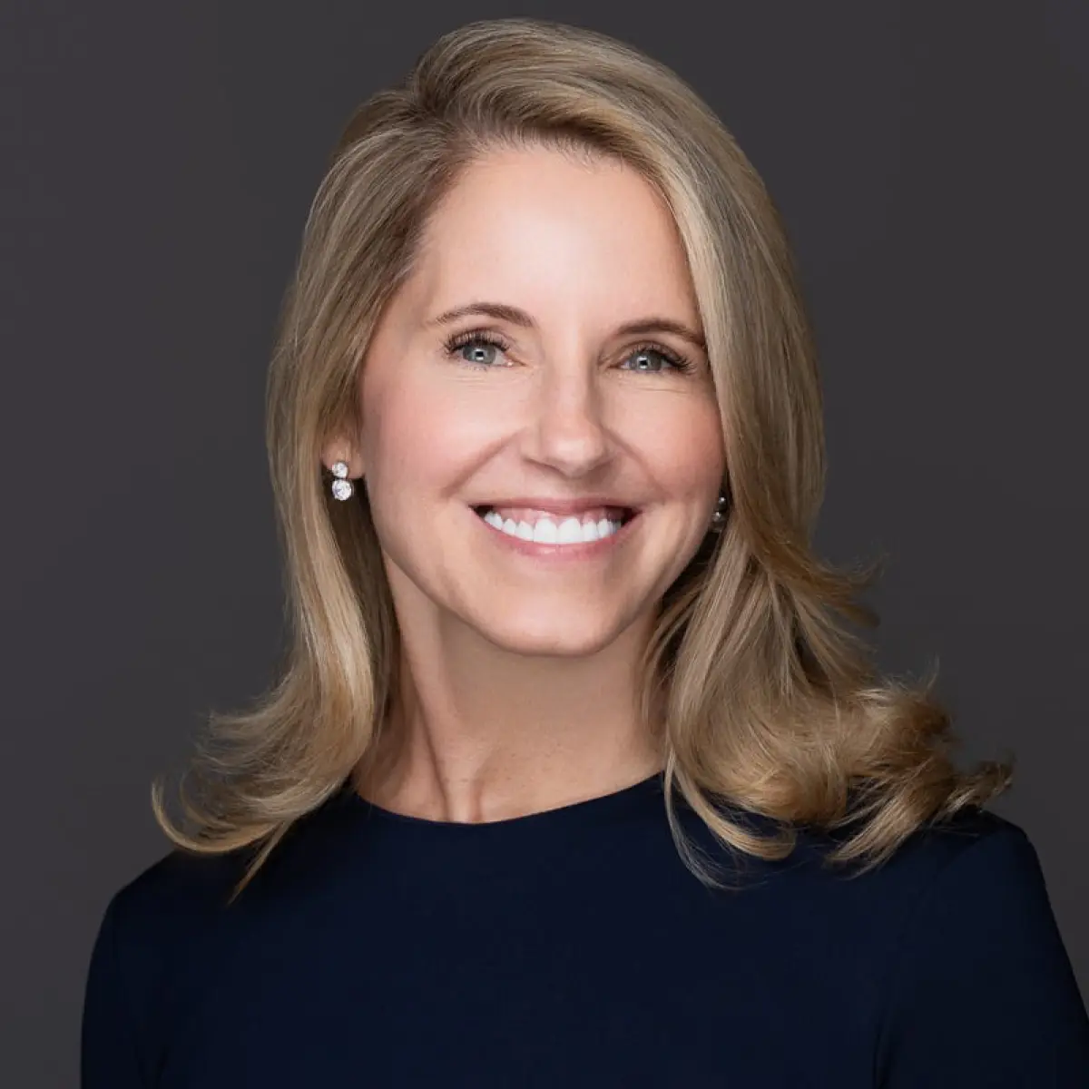 Portrait orientation photograph close-up headshot of Kristen (Kolensky) Waterfield smiling in a dark navy blue dress while wearing circular shaped chrome/silver earrings