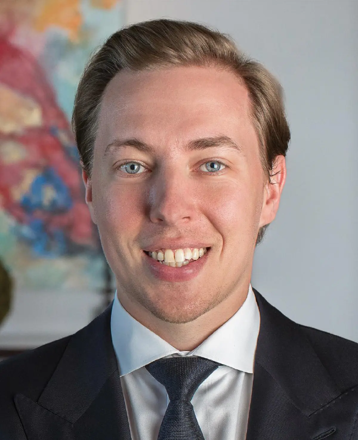 Portrait orientation photograph close-up headshot of Michael Wozniak smiling in a black business suit blazer with a white button-up dress shirt underneath as he has on a dark charcoal black tie equipped