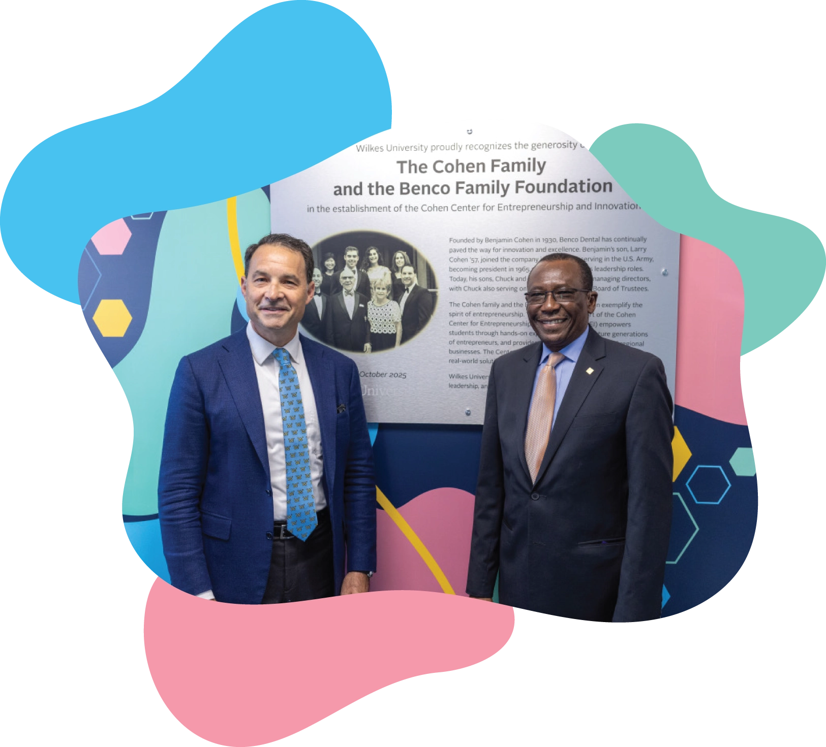 Chuck Cohen and Abel Adekola in suits standing in front of a plaque honoring the Cohen Family and Benco Family Foundation. The image is contained within a blue and pink abstract-shaped border.