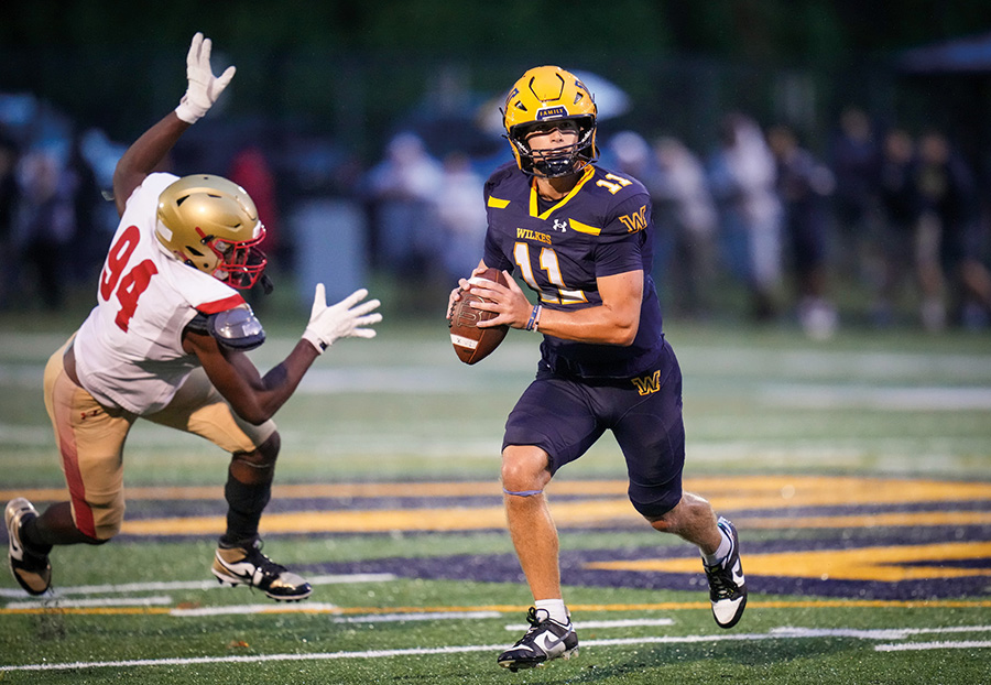 Wilkes University quarterback runs with the football while evading a defender during a game.