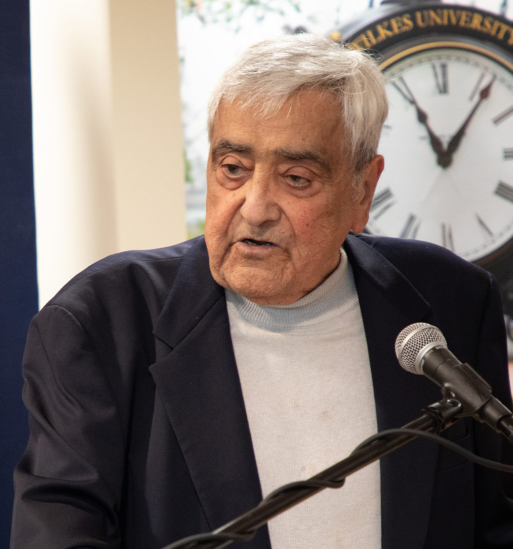 Dr. Alley speaking at a podium with a microphone, in front of a clock with Roman numerals.
